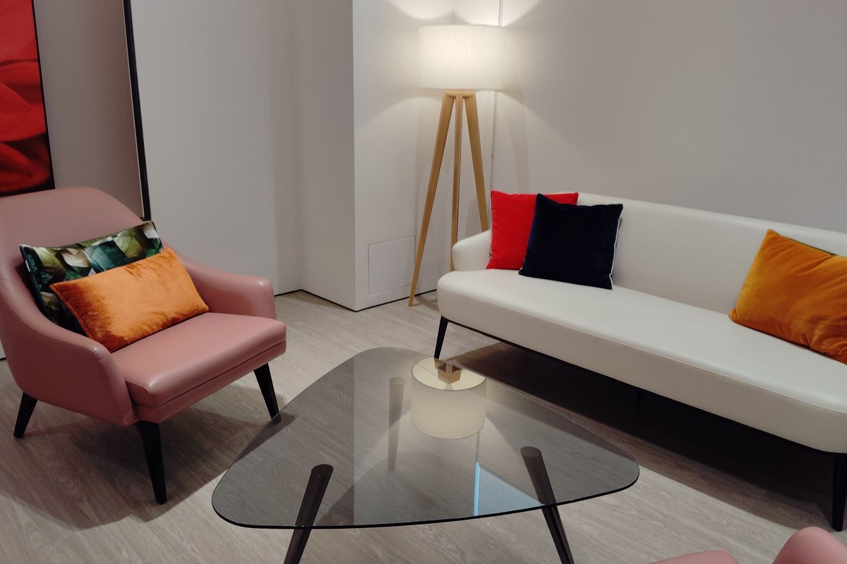 Cream leather sofa with colorful cushions, a pink armchair and a glass coffee table in a lit lounge