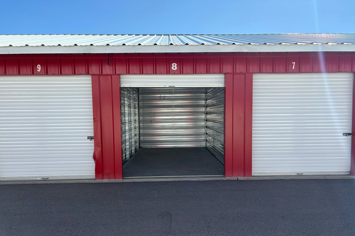 Row of storage units with white roll-up doors numbered 9, 8 and 7 in red trim, the middle door open on an empty unit