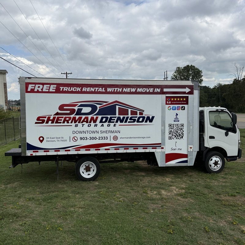 White box truck wrapped with Free Truck Rental With New Move In and the Sherman Denison Storage logo, parked on a lawn