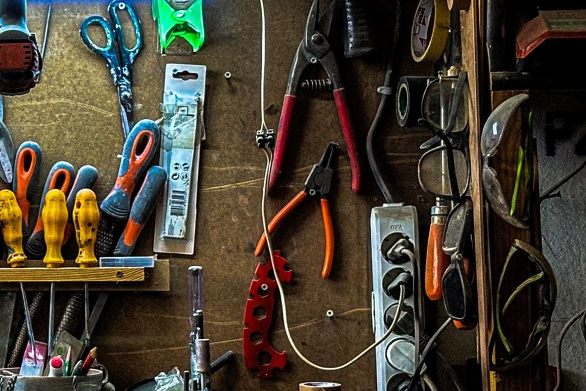 Screwdrivers, scissors, pliers and goggles hanging on a tool pegboard beside a power strip