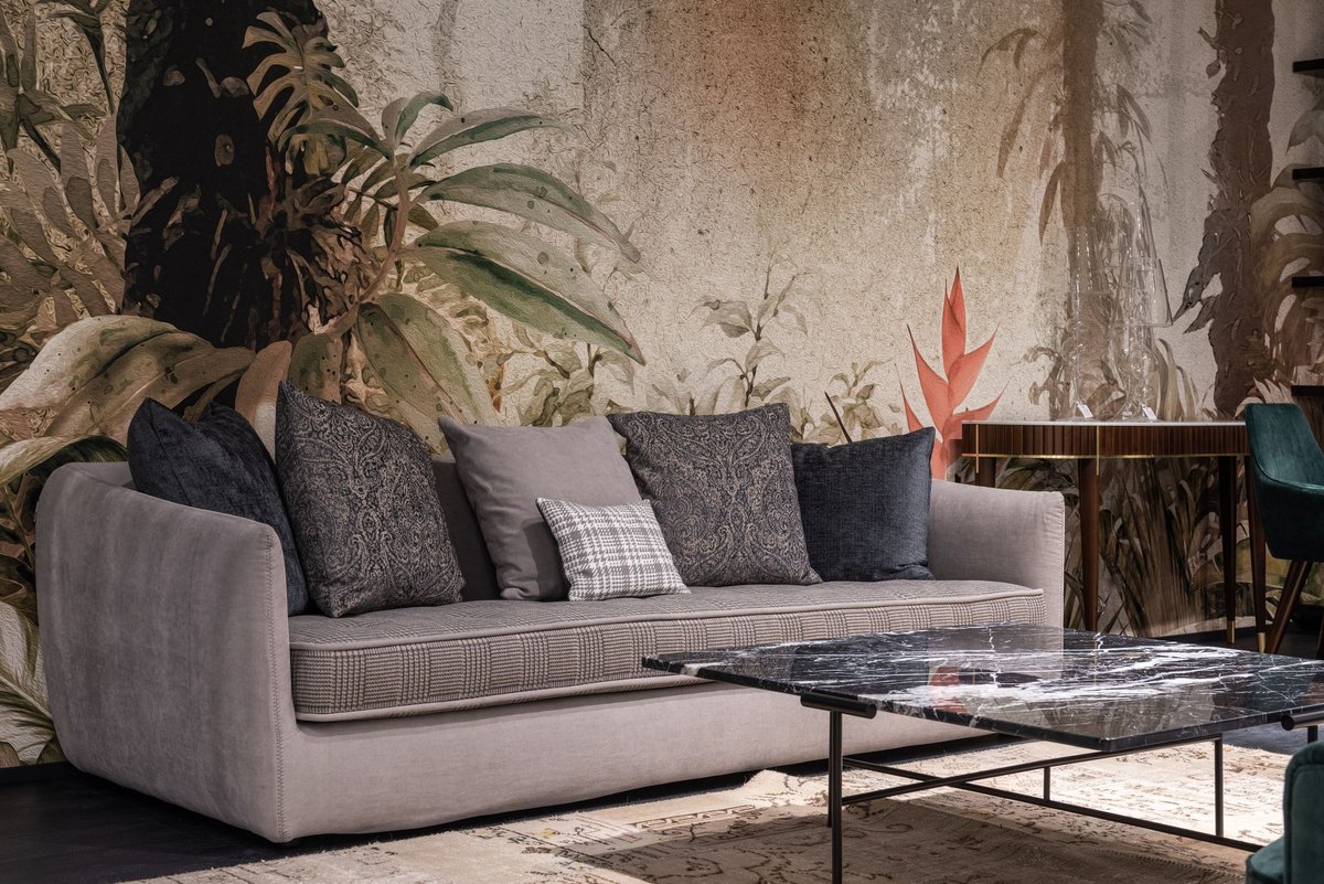 Gray sofa with gray and navy cushions in front of a leaf mural beside a black marble coffee table