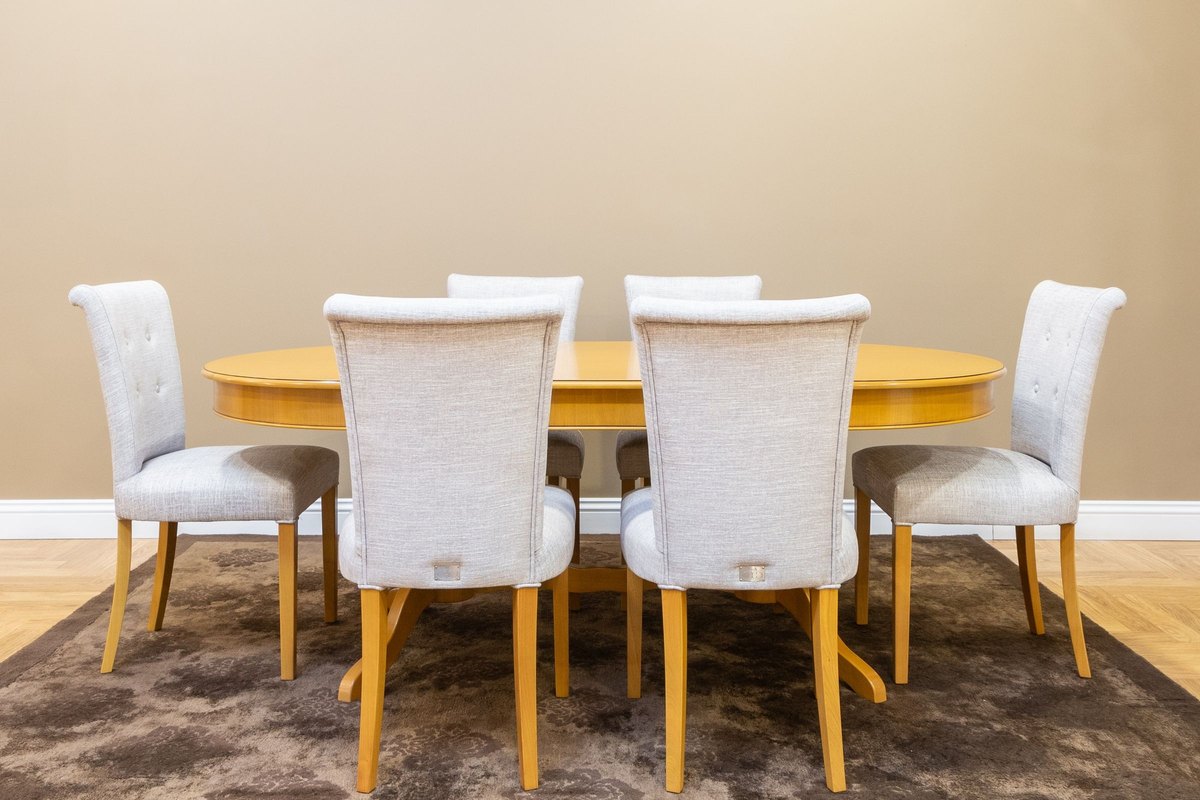 Oval wooden dining table with six gray upholstered chairs on a brown rug