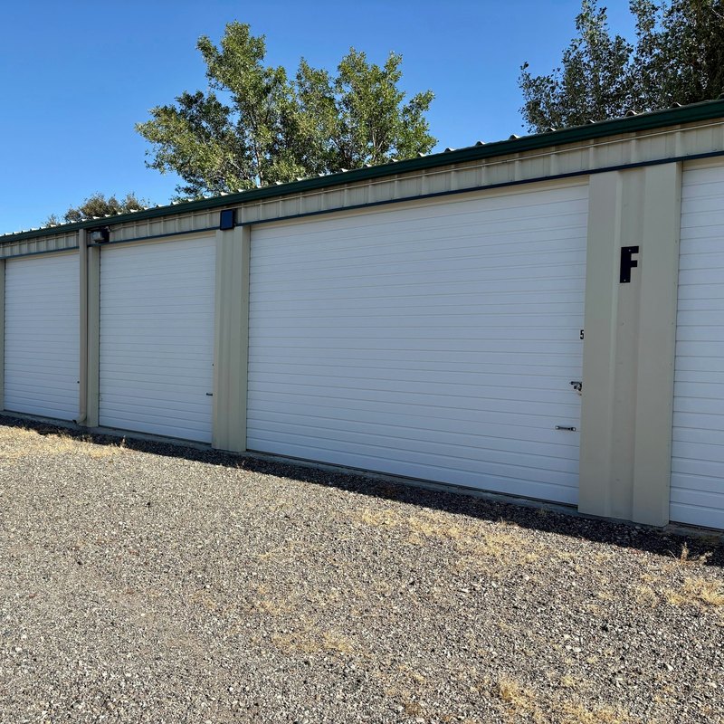 Beige metal storage building with white garage-style doors beside a gravel lot